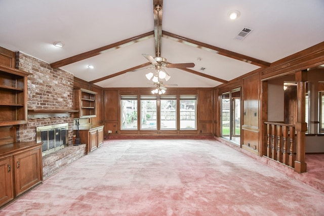 unfurnished living room with wood walls, lofted ceiling with beams, light colored carpet, ceiling fan, and a brick fireplace