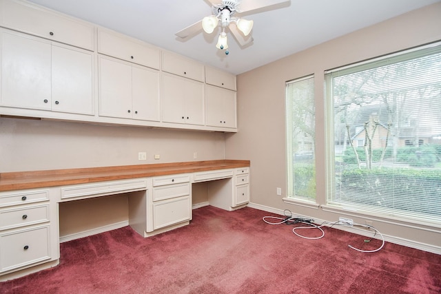 unfurnished office with ceiling fan, built in desk, and dark carpet