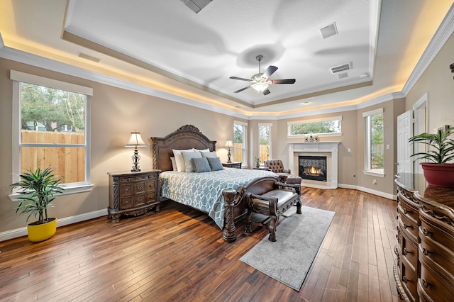 bedroom with visible vents, a raised ceiling, dark wood-style flooring, and a high end fireplace