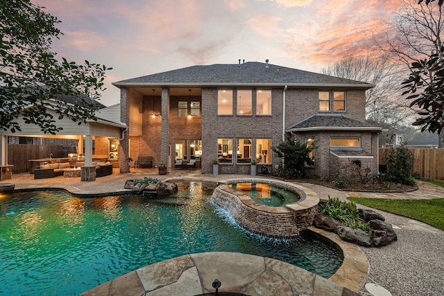 pool at dusk with a patio, a pool with connected hot tub, fence, and an outdoor living space