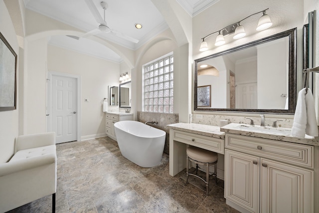 full bath featuring ceiling fan, ornamental molding, two vanities, a freestanding bath, and a sink