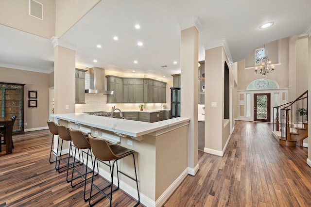 kitchen featuring decorative backsplash, a breakfast bar area, dark wood-type flooring, a peninsula, and wall chimney range hood