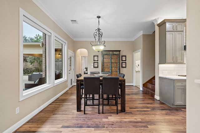 dining space featuring arched walkways, visible vents, baseboards, ornamental molding, and dark wood finished floors