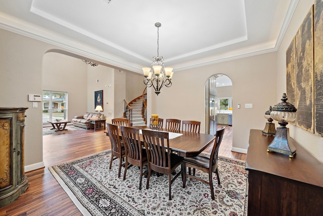 dining room with stairway, arched walkways, a tray ceiling, and wood finished floors