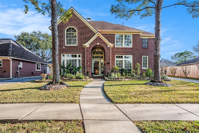 traditional home with brick siding, a chimney, a front yard, and fence