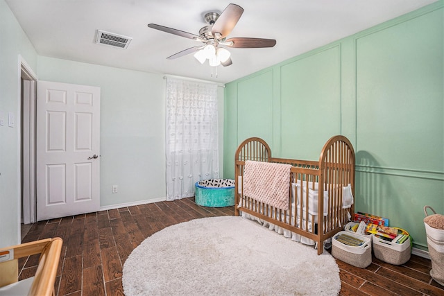 bedroom with dark wood-type flooring, ceiling fan, and a crib