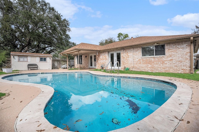 view of pool with french doors, a patio area, and an outbuilding