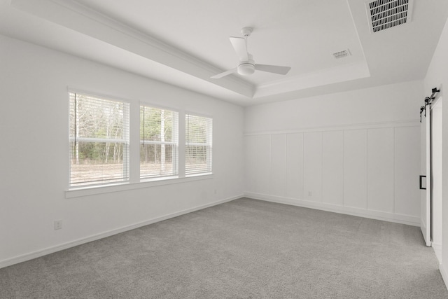 unfurnished room with a barn door, light carpet, ceiling fan, and a tray ceiling