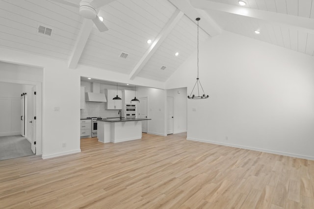 unfurnished living room featuring beamed ceiling, ceiling fan with notable chandelier, and light hardwood / wood-style floors