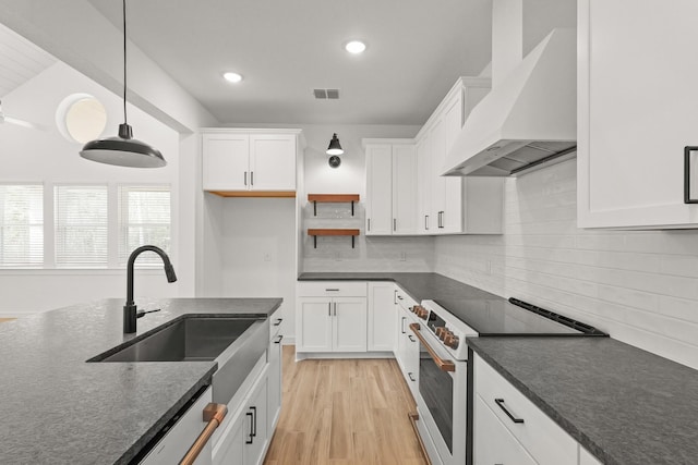 kitchen with pendant lighting, wall chimney range hood, sink, high end range, and white cabinetry