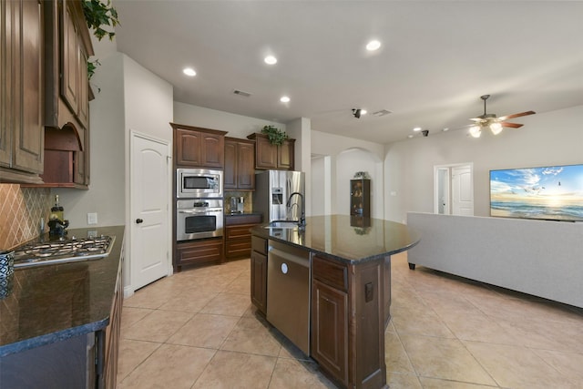 kitchen with sink, light tile patterned floors, appliances with stainless steel finishes, a kitchen island with sink, and decorative backsplash