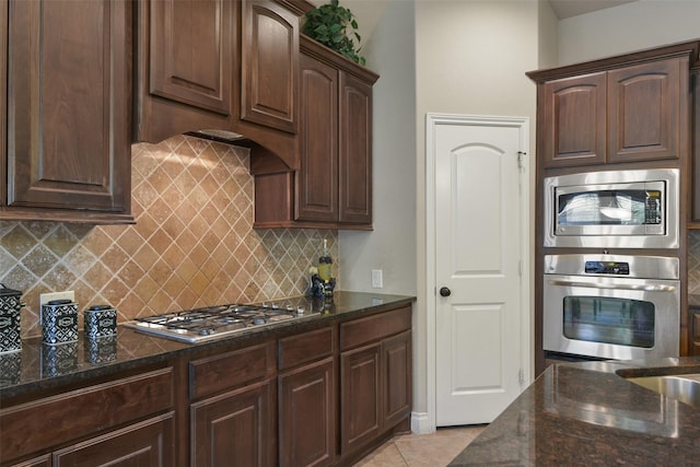 kitchen with dark stone counters, decorative backsplash, light tile patterned floors, stainless steel appliances, and dark brown cabinets