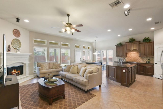 living room featuring ceiling fan, a fireplace, sink, and light tile patterned floors