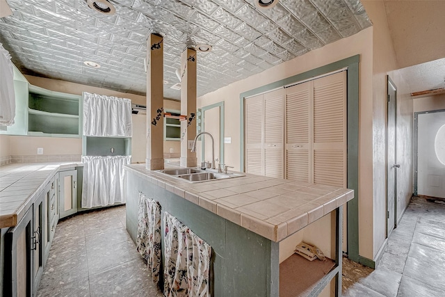 kitchen featuring tile counters, sink, and white cabinets