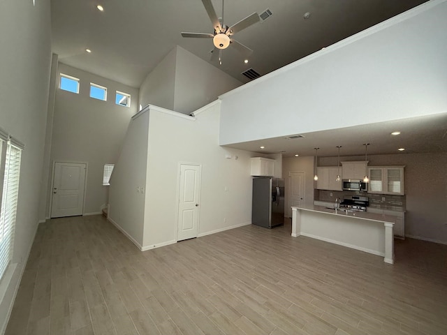 unfurnished living room with sink, a towering ceiling, ceiling fan, and light wood-type flooring