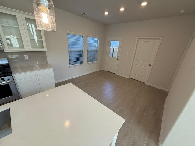 kitchen with hanging light fixtures, light hardwood / wood-style floors, white cabinets, decorative backsplash, and stainless steel range with gas cooktop