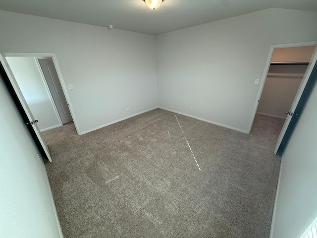 unfurnished bedroom featuring light carpet, a spacious closet, and vaulted ceiling