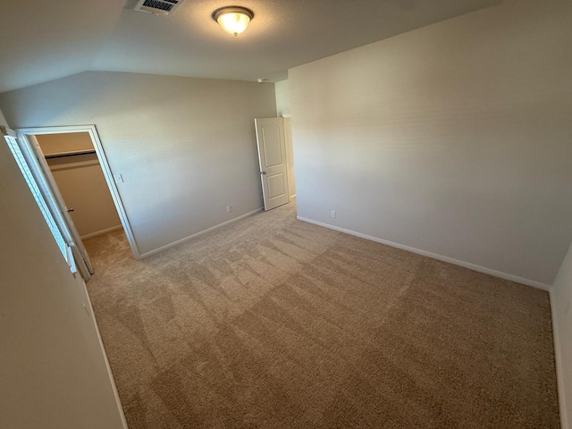 unfurnished bedroom featuring lofted ceiling, a walk in closet, light colored carpet, and a closet