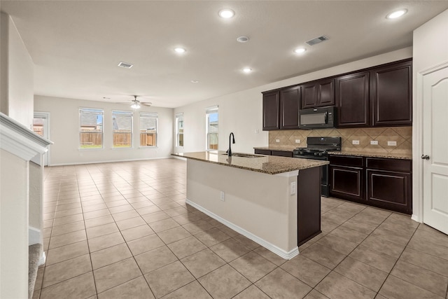 kitchen with sink, backsplash, light stone counters, range with gas stovetop, and an island with sink