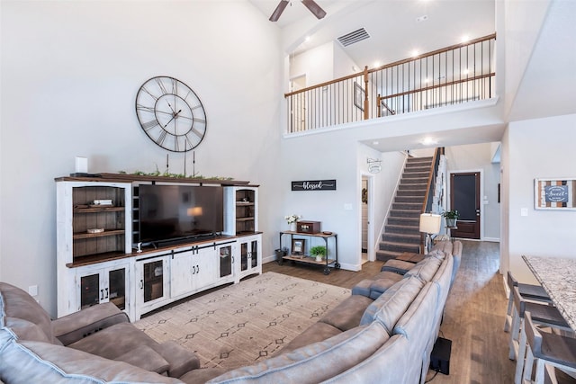 living room with hardwood / wood-style flooring, ceiling fan, and a towering ceiling