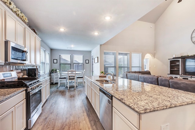 kitchen with sink, dark wood-type flooring, appliances with stainless steel finishes, light stone counters, and an island with sink