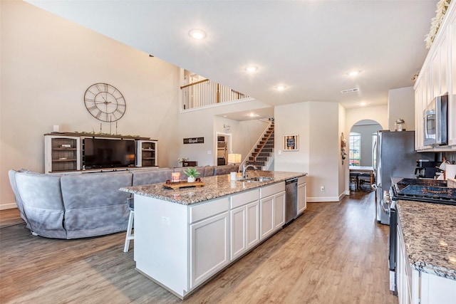 kitchen with light stone counters, appliances with stainless steel finishes, white cabinets, and a center island with sink