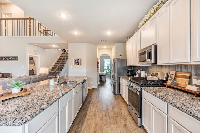 kitchen with appliances with stainless steel finishes, sink, white cabinets, light stone countertops, and light hardwood / wood-style flooring