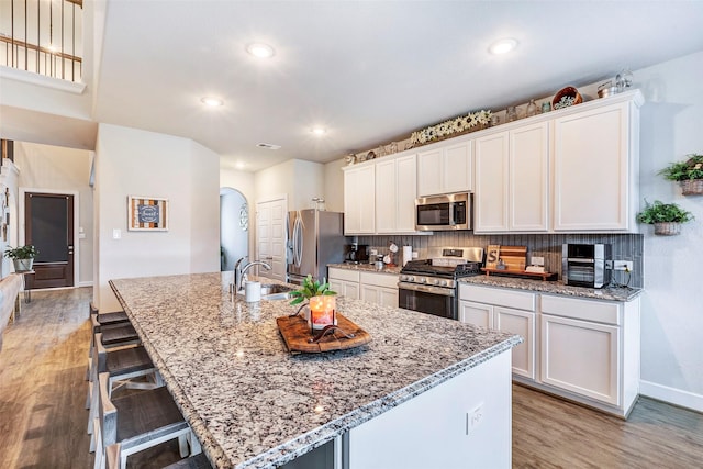 kitchen with appliances with stainless steel finishes, a kitchen bar, a kitchen island with sink, and white cabinets