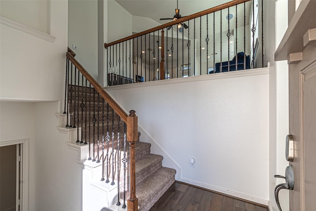 stairs with ceiling fan, wood-type flooring, and a high ceiling