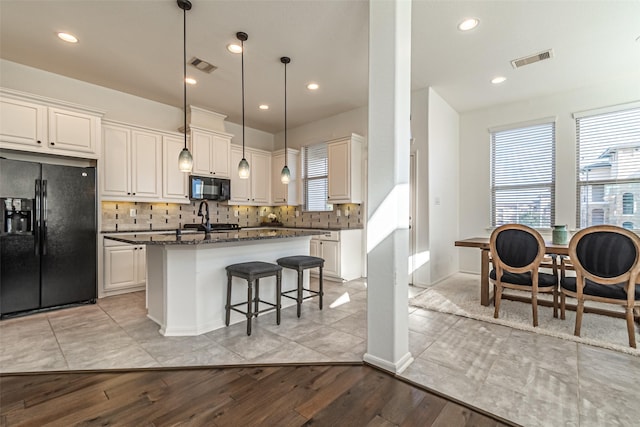 kitchen featuring white cabinetry, hanging light fixtures, a center island, black appliances, and dark stone counters