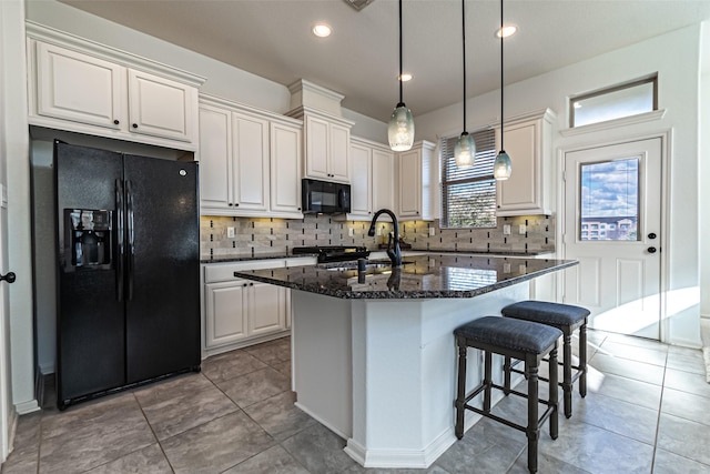 kitchen with an island with sink, white cabinets, dark stone counters, and black appliances