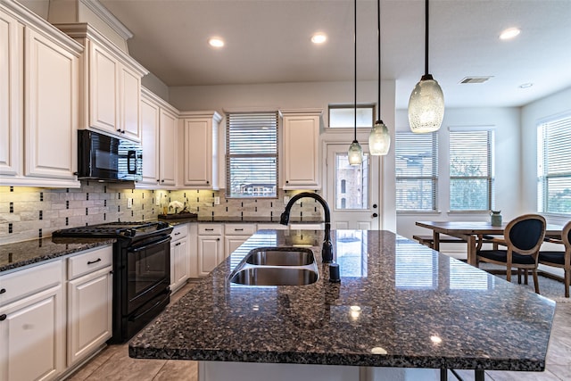 kitchen featuring sink, decorative light fixtures, an island with sink, dark stone counters, and black appliances