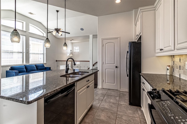 kitchen featuring sink, dark stone countertops, white cabinets, black appliances, and a center island with sink