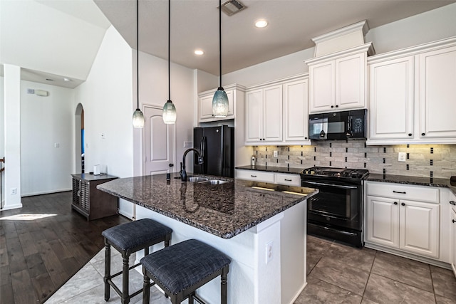 kitchen with a kitchen island with sink, sink, dark stone counters, and black appliances