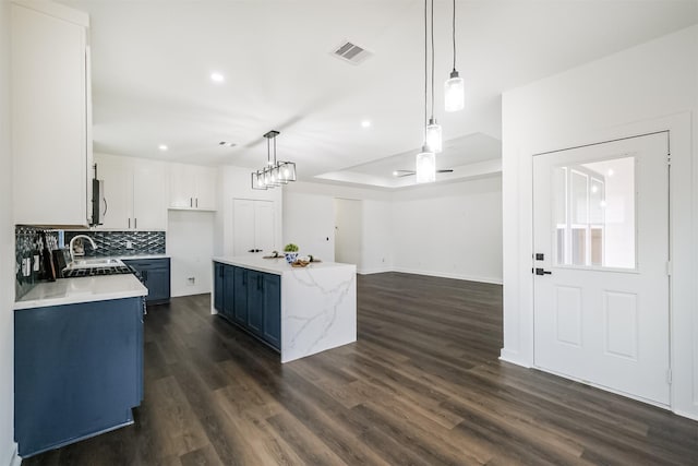 kitchen with dark wood-type flooring, white cabinetry, a kitchen island, blue cabinets, and decorative light fixtures