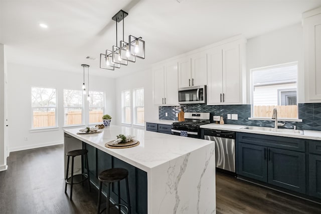 kitchen featuring sink, appliances with stainless steel finishes, white cabinetry, hanging light fixtures, and a center island