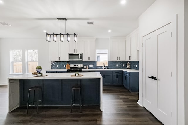 kitchen featuring white cabinetry, decorative light fixtures, a kitchen island, and appliances with stainless steel finishes