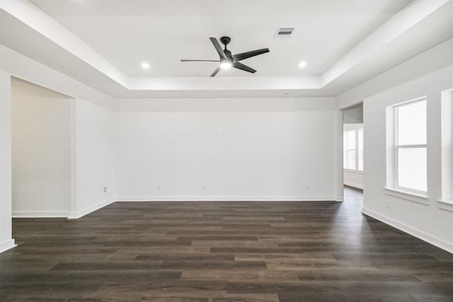 empty room featuring a tray ceiling, dark wood-type flooring, and ceiling fan