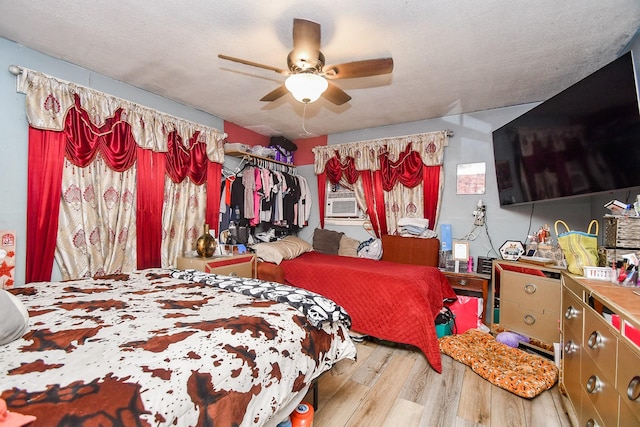 bedroom featuring cooling unit, ceiling fan, light hardwood / wood-style floors, and a textured ceiling