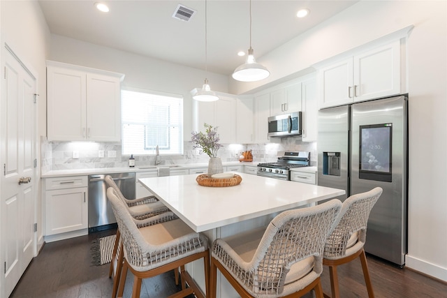 kitchen featuring stainless steel appliances, a kitchen island, pendant lighting, and white cabinets