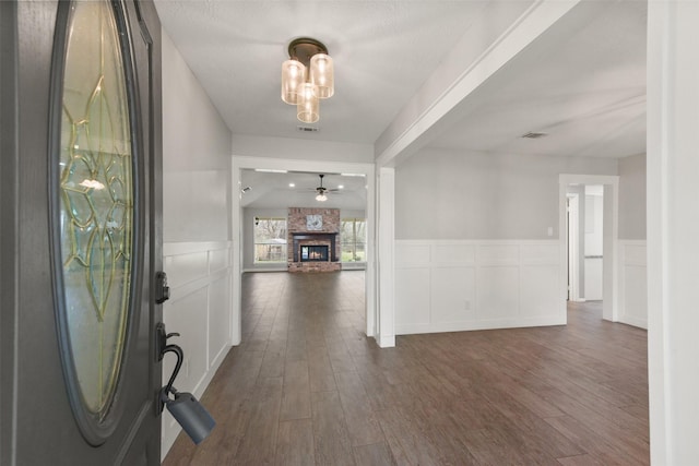 foyer featuring a large fireplace, dark wood-style flooring, and a wainscoted wall