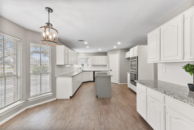 kitchen with hardwood / wood-style floors, double oven, white cabinets, backsplash, and light stone countertops