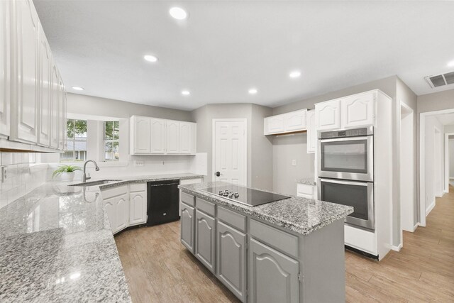 kitchen with sink, white cabinets, a center island, light stone counters, and black appliances