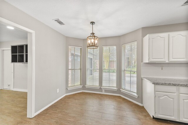 unfurnished dining area with a wealth of natural light, an inviting chandelier, and light hardwood / wood-style floors