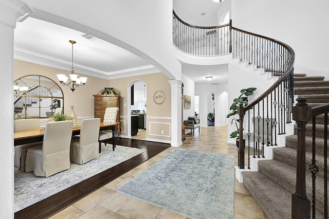 foyer with crown molding, ornate columns, a chandelier, and a towering ceiling