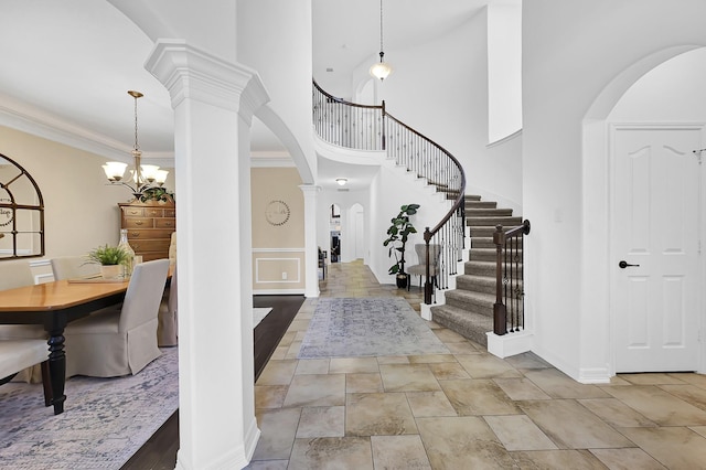 foyer entrance with crown molding, ornate columns, a high ceiling, and a notable chandelier