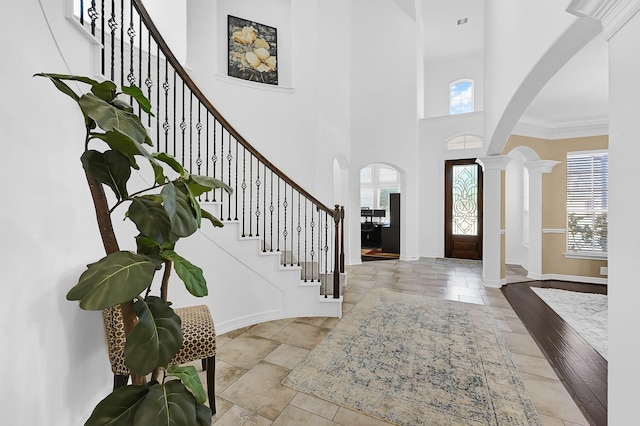 foyer with light tile patterned floors, a towering ceiling, decorative columns, and a healthy amount of sunlight