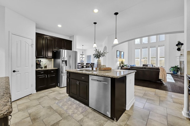 kitchen featuring decorative light fixtures, an island with sink, sink, light stone counters, and stainless steel appliances