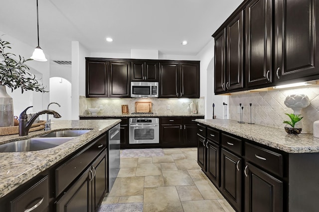 kitchen featuring appliances with stainless steel finishes, pendant lighting, sink, backsplash, and light stone counters