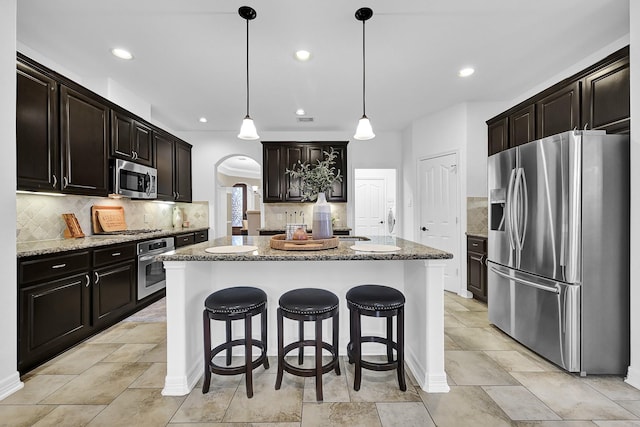 kitchen featuring a kitchen island, stone countertops, pendant lighting, a breakfast bar area, and stainless steel appliances